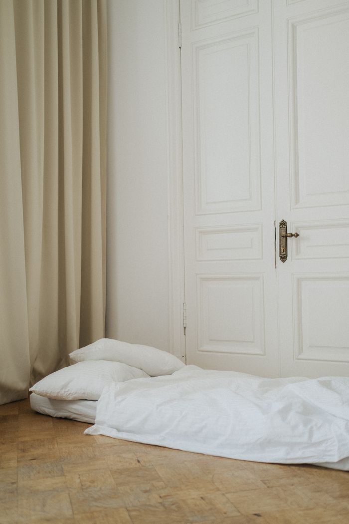Cozy bedroom with white bedding against a closed door and elegant curtains on a wooden floor.